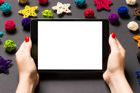 Top view of woman holding tablet in her hands on black background made of Christmas decorations. New...