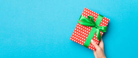 Woman arms holding gift box with colored ribbon on blue table background, top view and copy space...