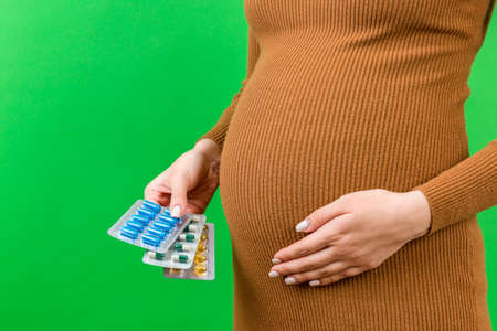 Cropped image of pregnant woman holding pill blisters at colorful background with copy space. Medical problems during pregnancy concept.の写真素材