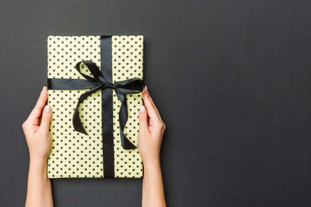 Top view of female hands holding christmas or other holiday handmade present box package in the palms, flat lay on black background with copy space.の写真素材