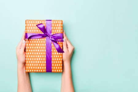 Woman hands give wrapped christmas or other holiday handmade present in colored paper. Present box, decoration of gift on Blue table, top view with copy space.の写真素材
