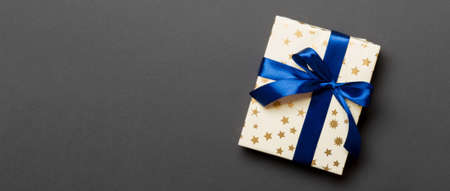 wrapped Christmas or other holiday handmade present in paper with blue ribbon on black background. Present box, decoration of gift on colored table, top view with copy space.の写真素材