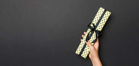 Top view of female hands holding christmas or other holiday handmade present box package in the palms, flat lay on black background with copy space.の写真素材