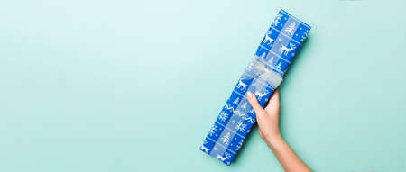 Woman hands give wrapped christmas or other holiday handmade present in colored paper. Present box, decoration of gift on Blue table, top view with copy space.の写真素材