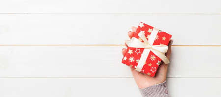 Female hands holding present on white wooden background. Festive backdrop for Christmas holidays or...