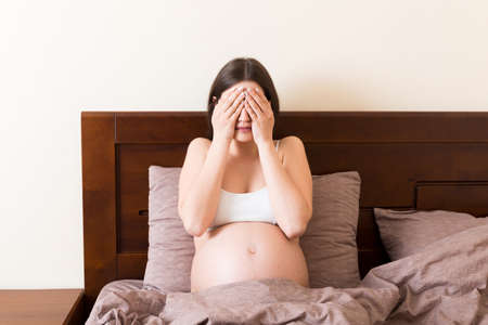 Young pretty pregnant woman suffering from headache at home in bed.の写真素材