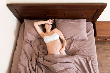 beautiful young pregnant woman lying in bed, top view. the girl suffers from the fact that her husband left her,の写真素材