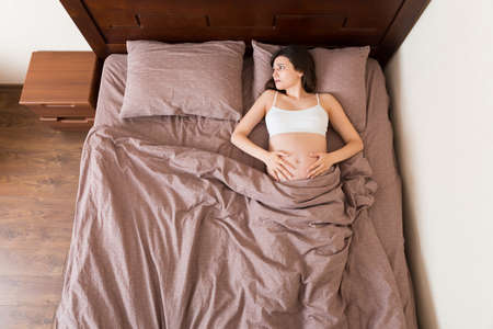 beautiful young pregnant woman lying in bed, top view. the girl suffers from the fact that her...