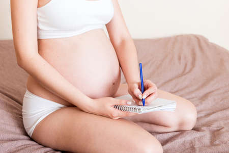 Pregnant woman makes notes in notebook. Concept of pregnancy Mother waiting for baby.の写真素材
