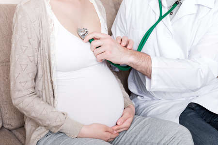 Doctor is checking pregnant woman's heartbeat with a stethoscope.の写真素材