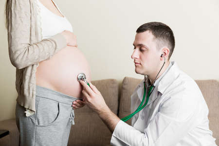 Doctor is checking pregnant woman's belly with a stethoscope. Physician is listening to a heartbeat of a baby.の写真素材