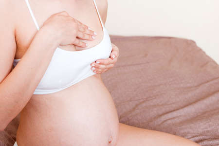 Close Up of pregnant women having painful feelings in breast. Woman checking her breast for cancer.
