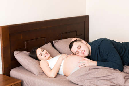 Pregnant woman with her husband in bed in the morning.の写真素材