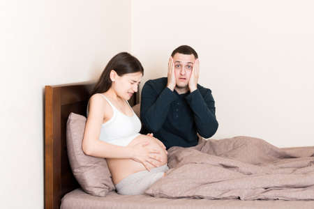 husband shocked while his pregnant wife has contractions on bed in home.の写真素材
