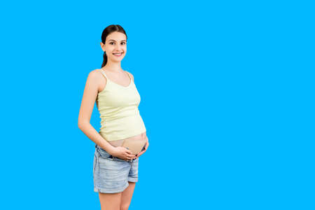 Portrait of pregnant woman wearing pregnancy corset against backpain at blue background with copy...