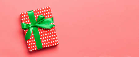 Top view Christmas present box with green bow on living coral background with copy space.