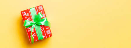 wrapped Christmas or other holiday handmade present in paper with green ribbon on yellow background. Present box, decoration of gift on colored table, top view with copy space.の写真素材