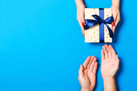 Top view of a gift in male and female hands on colorful background. Congratulation of each other concept. Close up.の写真素材