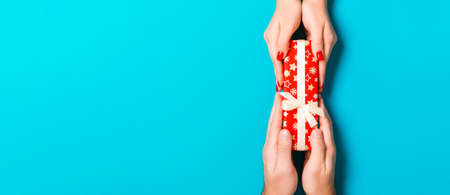 Top view of male and female hands holding present box on colorful background. Sharing a gift concept. Close up.の写真素材