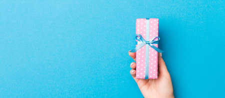 Woman arms holding gift box with colored ribbon on blue table background, top view and copy space...