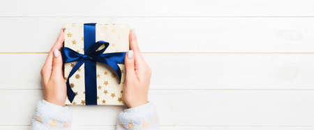 Woman hands give wrapped christmas or other holiday handmade present in colored paper. Present box,...