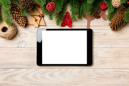 Top view of tablet, Christmas toys, decorations and fir tree branches on wooden background. New Year...