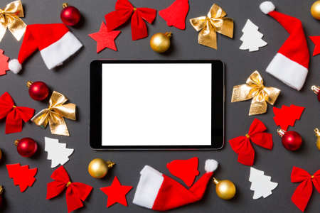 Top view of digital tablet on black background with New Year toys and decorations. Christmas time...