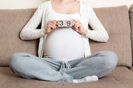 Pregnant woman in white underwear on bed in home holding calendar with weeks 39 of pregnant....