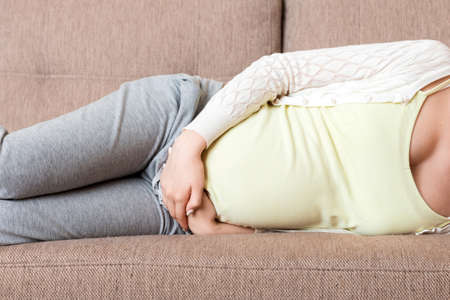 Beautiful pregnant woman suffering belly ache lying on a sofa at home.の写真素材