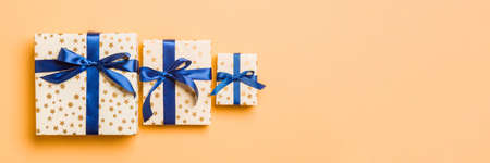 Top view Christmas present box with blue bow on orange background.