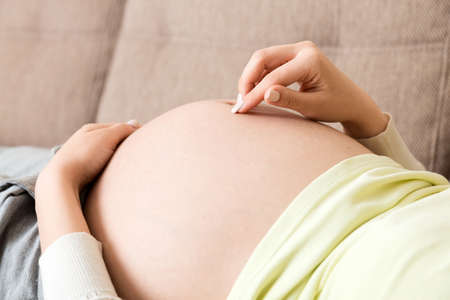 pregnant woman on sofa and touching her belly at home. pregnancy expectation concept.