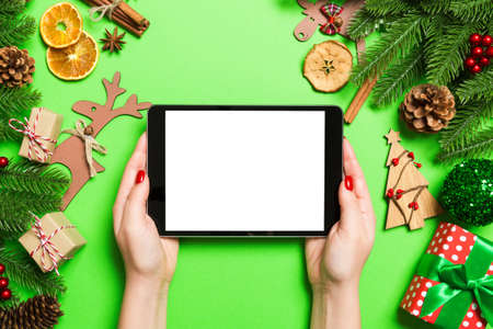 Top view of woman holding tablet in her hands on green background made of Christmas decorations. New...