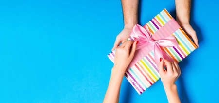Top view of giving a present to a lovely person on colorful background. Couple congratulate each...