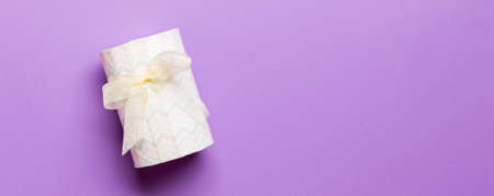 Top view Christmas present box with yellow bow on purple background with copy space.