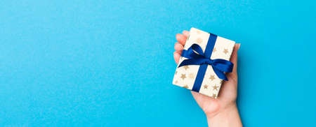 Woman arms holding gift box with colored ribbon on blue table background, top view and copy space...