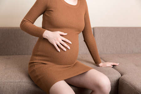 Pregnant Lady Having Massaging Lower belly Sitting On Sofa Indoor. Pregnancy Problems Concept....