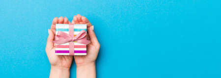 Woman arms holding gift box with colored ribbon on blue table background, top view and copy space for you design.の写真素材
