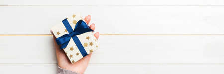 Woman arms holding gift box with colored ribbon on white wooden table background, top view copy space.の写真素材