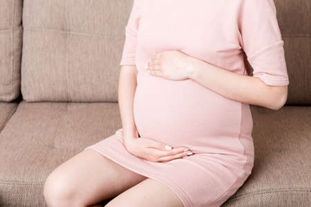 Pregnant Lady Having Massaging Lower belly Sitting On Sofa Indoor. Pregnancy Problems Concept....