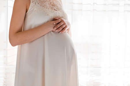 Pretty young pregnant woman standing by the window in home.の写真素材