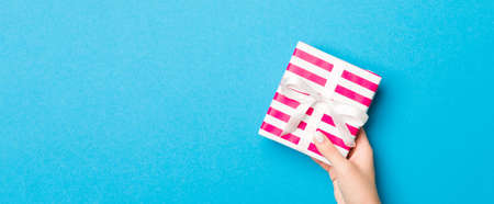 Woman arms holding gift box with colored ribbon on blue table background, top view and copy space...