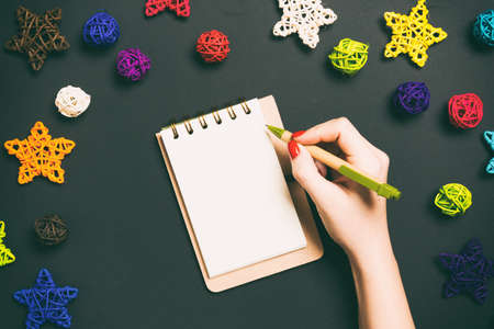 Top view of female hand making some notes in noteebok on colorful background. New Year decorations...