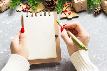 Top view of female hand writing in a notebook on cement Christmas background. fir tree and festive decorations. Wish list. New Year concept.の写真素材
