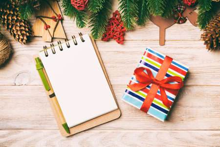 Top view of gift, notebook, Christmas toys, decorations and fir tree branches on wooden background....