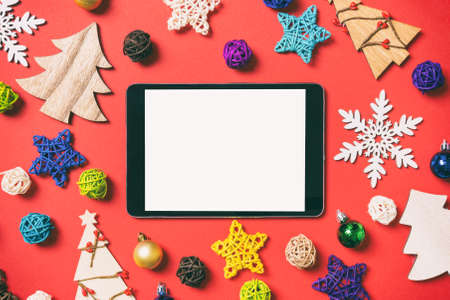 Top view of digital tablet on red background made of holiday decorations and toys. Christmas ornament concept.の写真素材