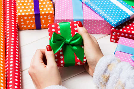 Top view of female hand tie up New Year present on festive wooden background. Gift boxes and rolled...