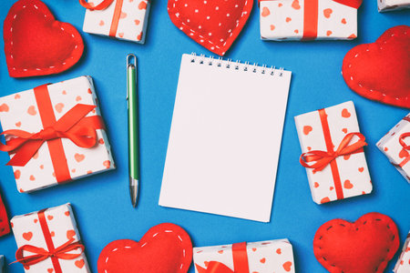 Top view of notebook, white gift boxes and red textile hearts on colorful background. Valentine's Day concept.の写真素材