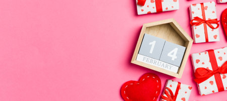 Holiday composition of gift boxes, wooden calendar and red textile hearts on colorful background...