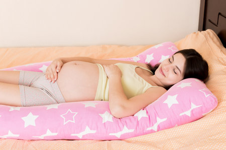 Beautiful pregnant woman sleeping with body pillow on bed.の写真素材