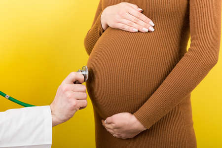 Closeup of doctor examining pregnant woman on colorful background.
